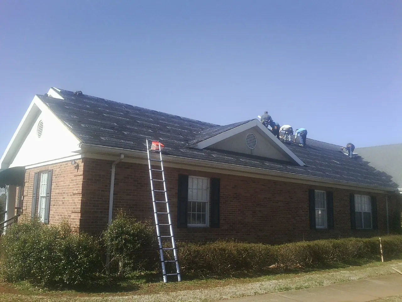 Crew tearing shingles off a brick ranch roof with a ladder set — Metal Roof Repair work by our crew in Dixon