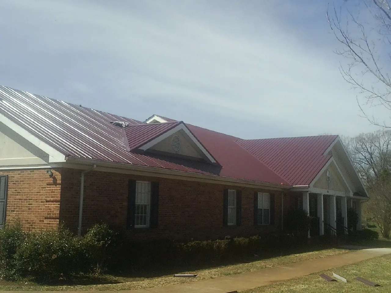 Red metal roof with gabled entries on a long brick building, from a Hail Damage Roof Repair job in Dixon