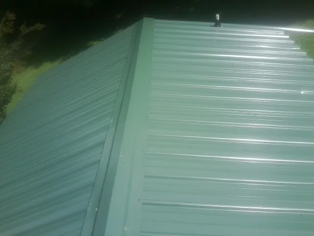 New green metal panels meeting at the ridge of a roof — Flat Roof Repair work by our crew in Dixon